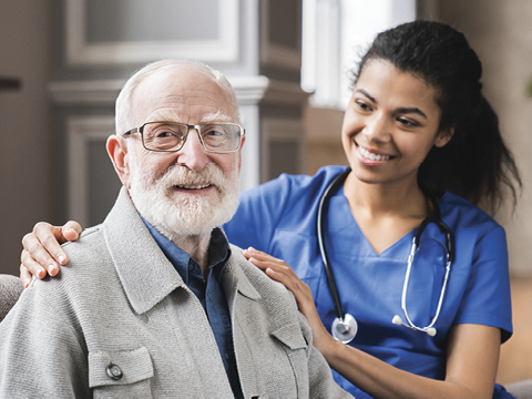 young nurse in blue coat hugging old 80s man smiling looking at camera